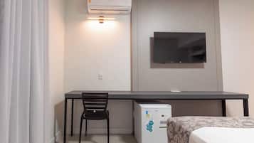 A hotel room with a bed, a desk with a chair, a television mounted on the wall, and a minibar.