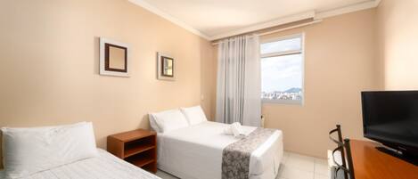 Habitación de hotel con dos camas, un televisor, una ventana con vista a la ciudad y un escritorio de madera.