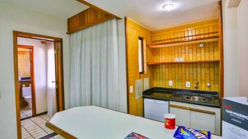 Una habitación de hotel pequeña con una cama, una kitchenette y un baño visible a través de una puerta abierta.
