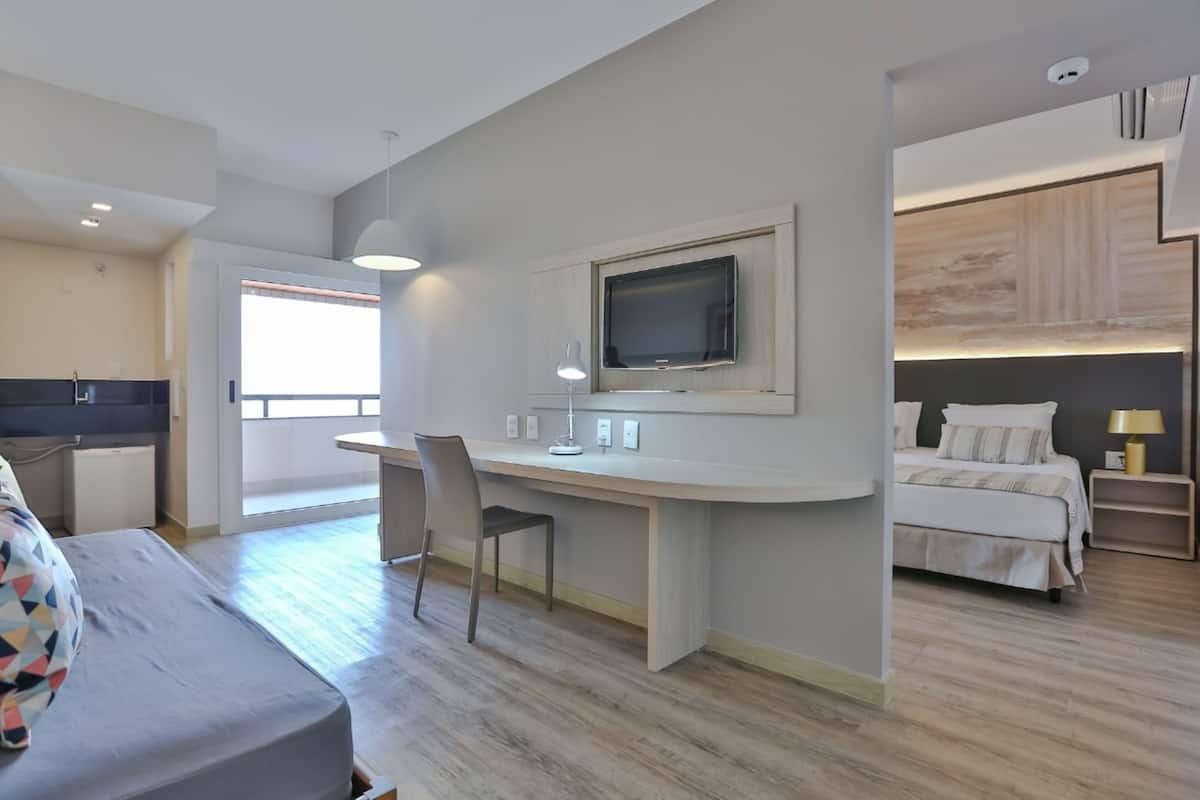 Une chambre d’hôtel moderne comprenant un lit, un bureau avec une télévision, une chaise et une petite table.
