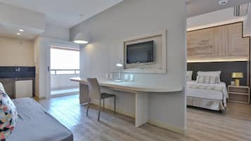 A modern hotel room with a bed, a desk with a TV, a chair, and a small table.