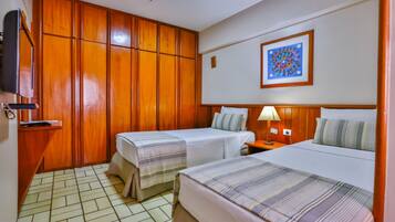 A hotel room with two single beds, a wooden wardrobe, a television, and a framed picture on the wall.