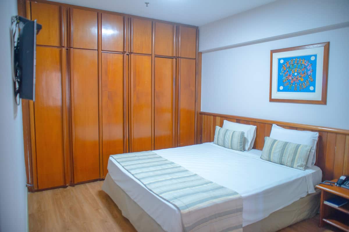 Une chambre avec un grand lit, une armoire en bois et un tableau encadré accroché au mur.