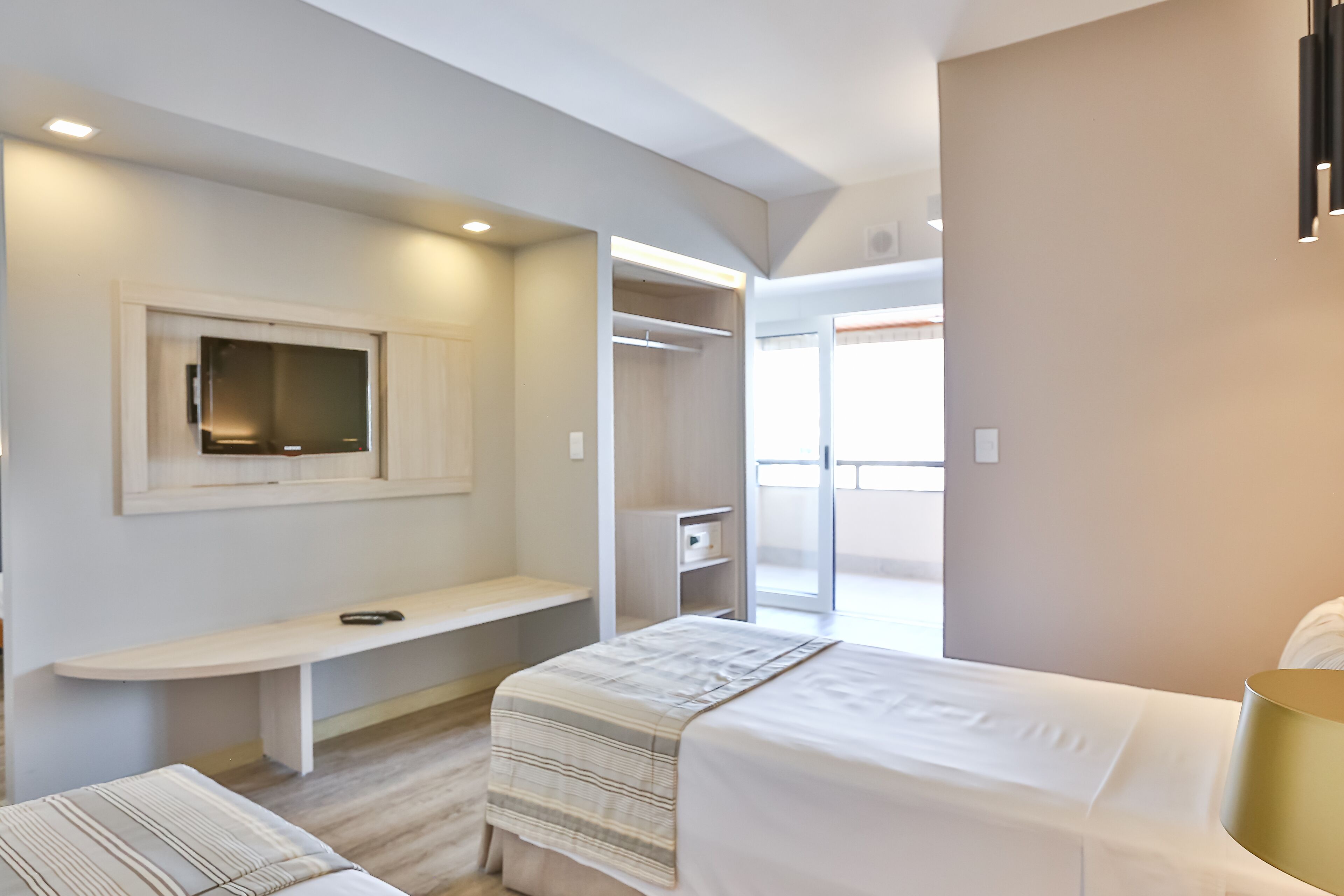 A modern hotel room with a bed, a desk, a TV, a closet, and a balcony.
