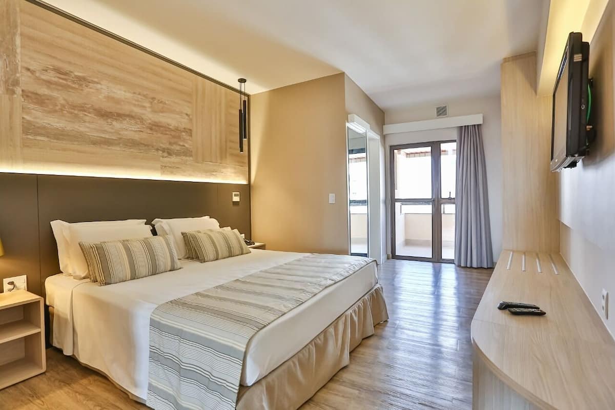 Une chambre d’hôtel moderne avec un grand lit, un bureau et un téléviseur fixé au mur.