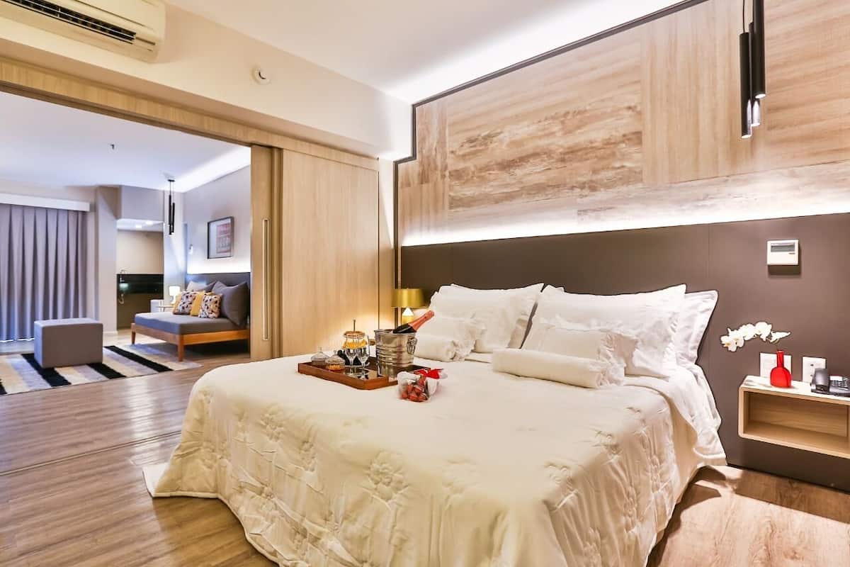 Une chambre d’hôtel moderne avec un grand lit, des tables de chevet, une petite table et une vue sur la chambre voisine.
