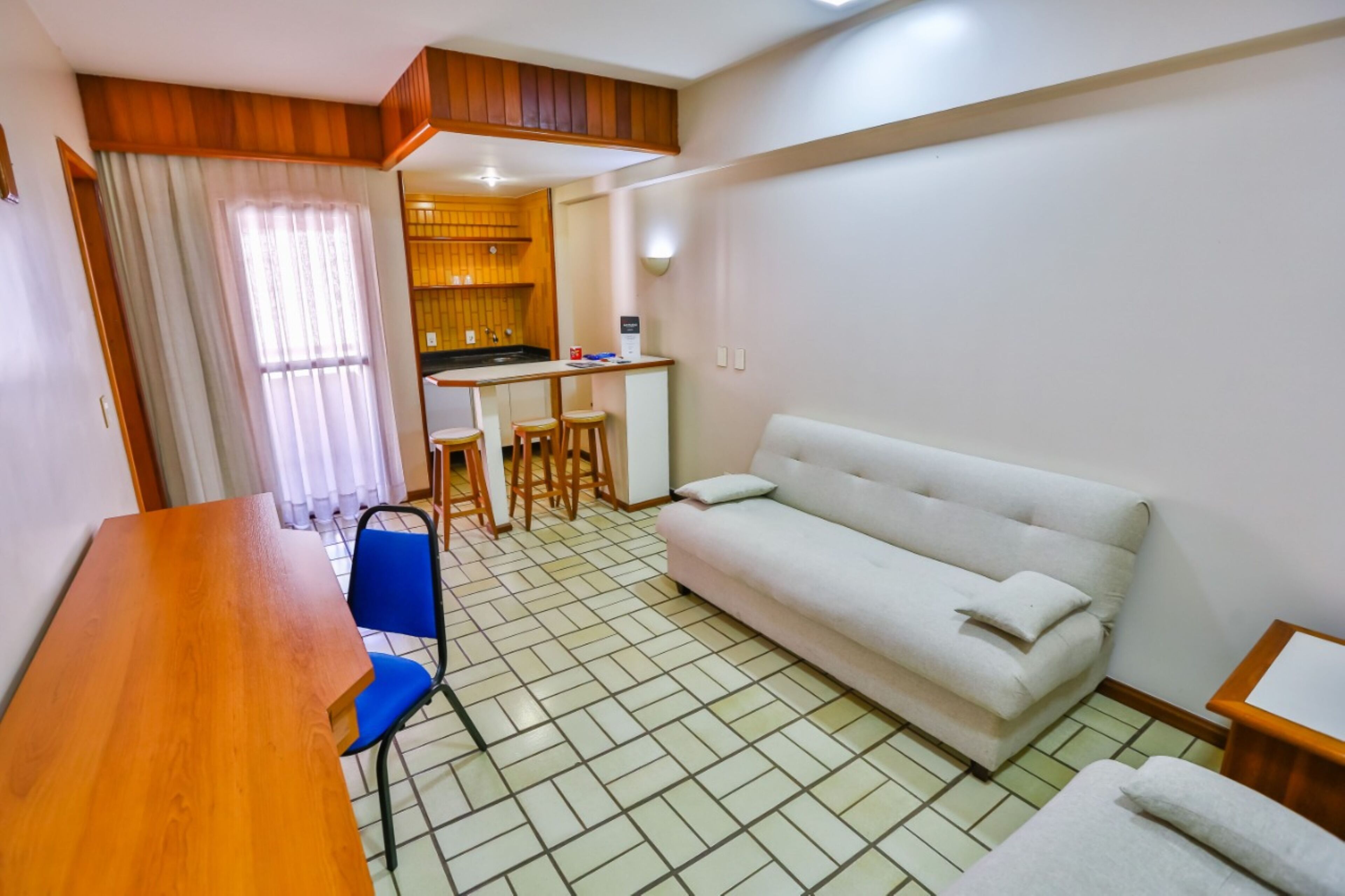 Um espaço compacto para viver com cozinha compacta, sofá, mesa de jantar e uma cadeira azul.