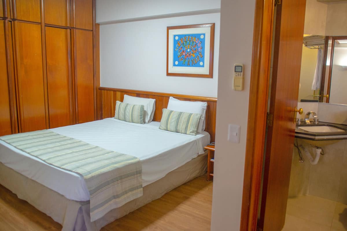 Une chambre à coucher bien rangée, avec un grand lit, deux oreillers, une table de chevet et un tableau encadré accroché au mur.