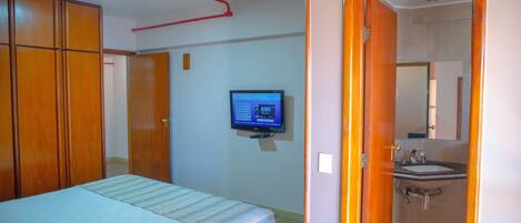A bedroom with a bed, a television, and a bathroom with a sink and mirror.
