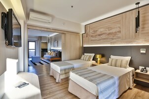 Habitación de hotel con dos camas, un televisor de pantalla plana montado en la pared, una mesita de noche con lámpara y vistas al pasillo.