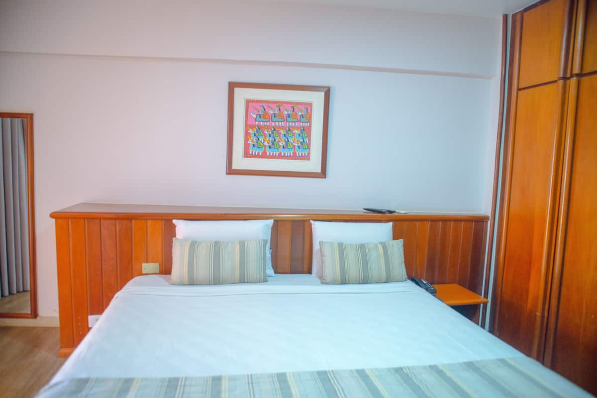 Une chambre d’hôtel avec un lit, une tête de lit en bois, un tableau encadré au mur et une armoire en bois.