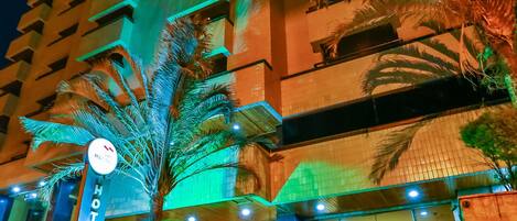 Un hotel con fachada moderna, una palmera y un cartel que indica que es un hotel.