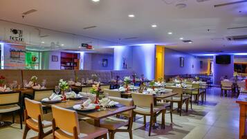 A restaurant with multiple dining tables and chairs, some with floral centerpieces.