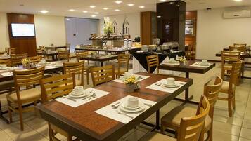Uma sala de jantar com várias mesas postas, cadeiras e um buffet ao fundo.