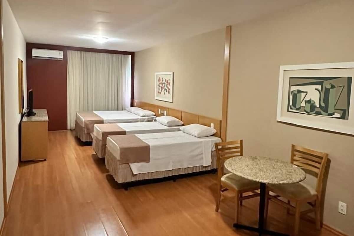 Ett hotellrum med två separata sängar, ett litet bord med stolar, ett skrivbord med en stol, en takfläkt och konstverk på väggarna.