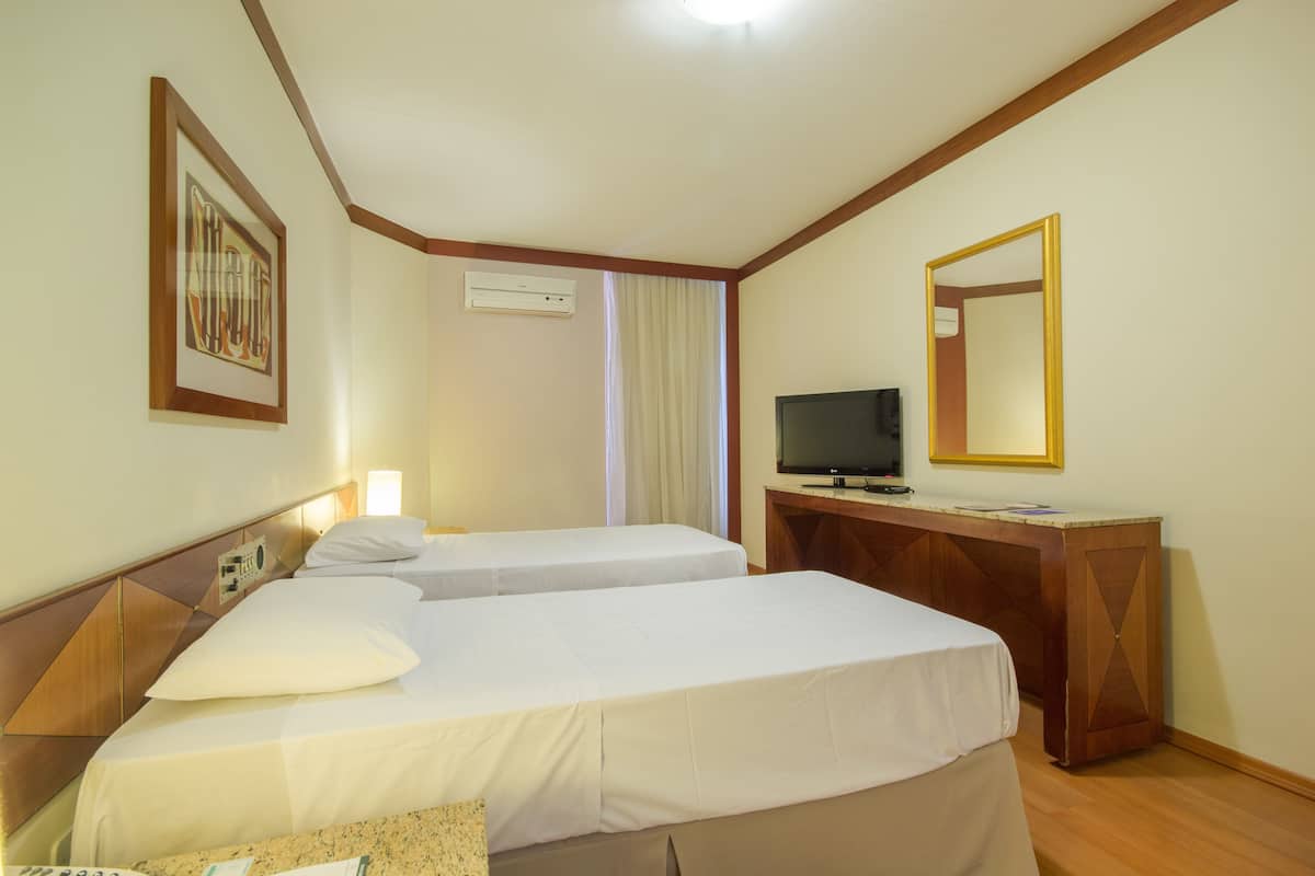 Ett hotellrum med två sängar, ett skrivbord med en tv, en spegel och en luftkonditioneringsanläggning.