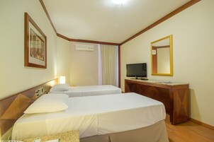 A hotel room with two beds, a desk with a television, a mirror, and an air conditioning unit.