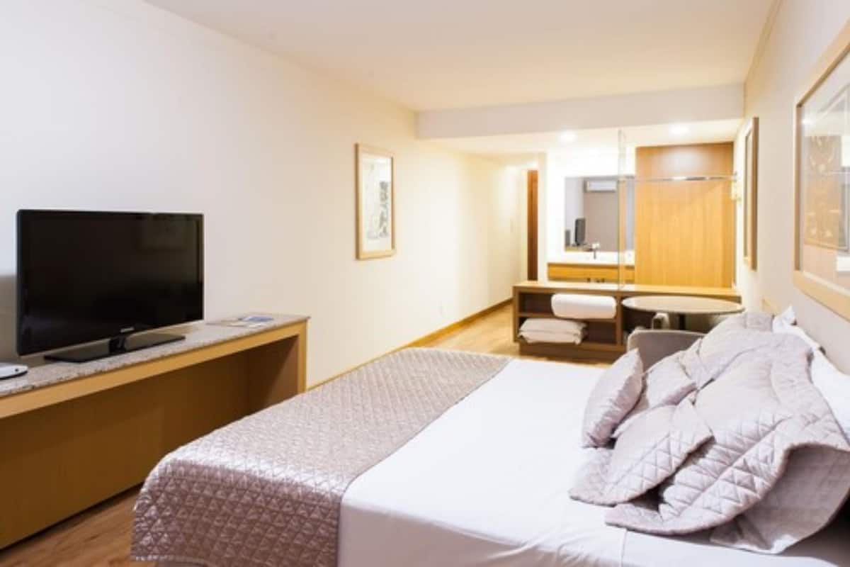 Ett hotellrum med en säng, en tv på ett skrivbord, ett badrum med en spegel och ett träskåp.
