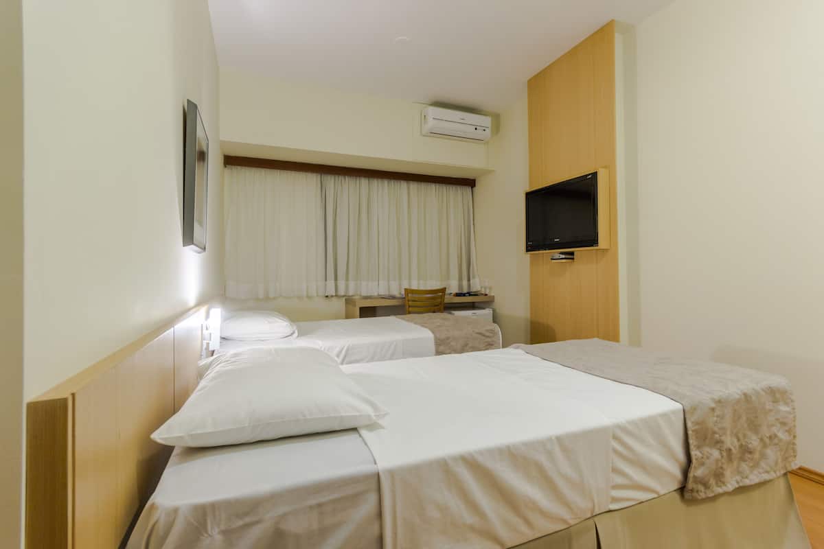 Ett hotellrum med två separata sängar, ett skrivbord, en stol, en tv och en luftkonditioneringsanläggning.