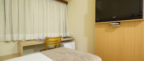 A hotel room with a bed, a desk, a chair, a television, and a small refrigerator.