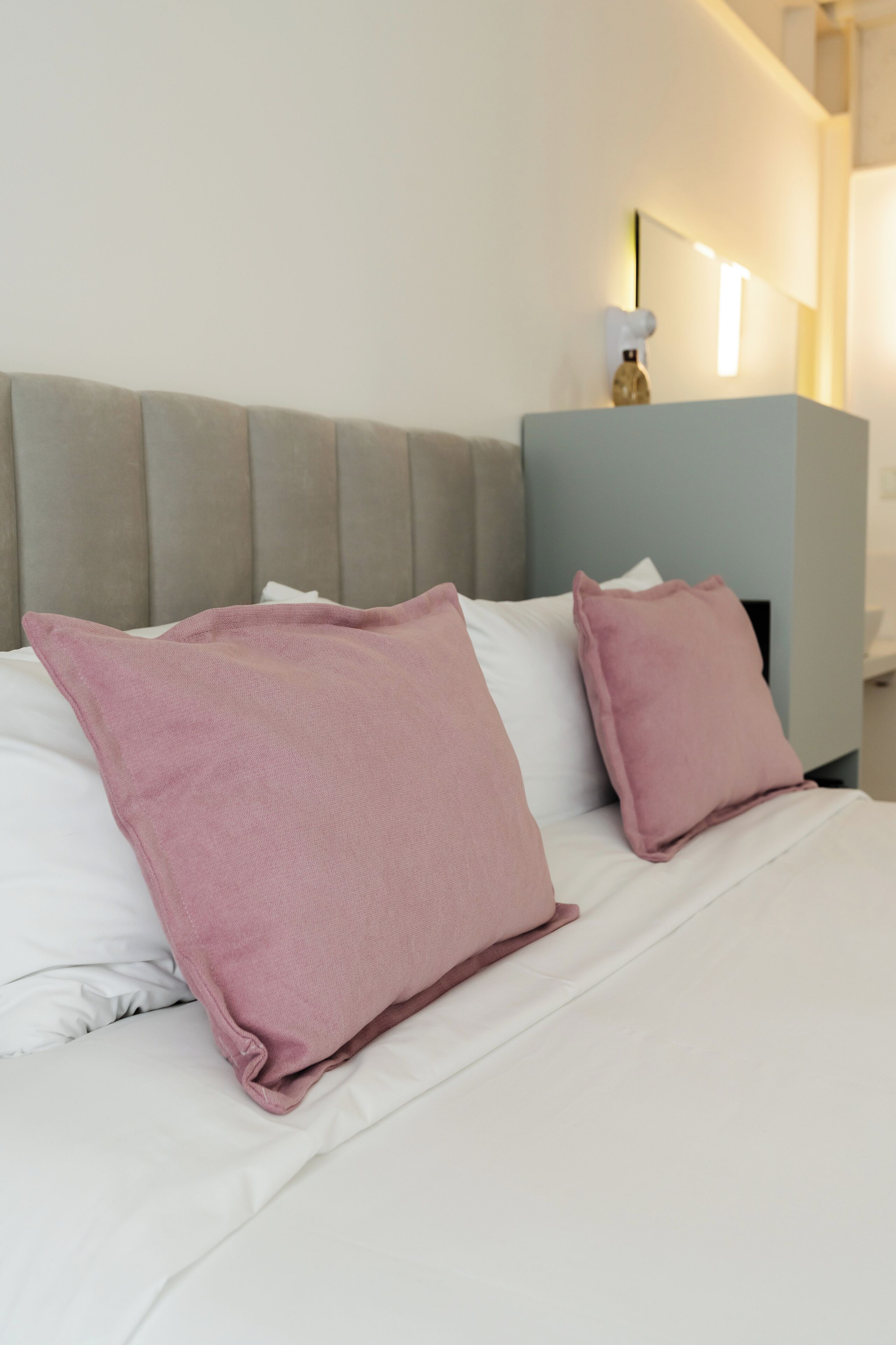 A neatly made bed with white and pink pillows, a light blue headboard, and a wall-mounted light fixture.