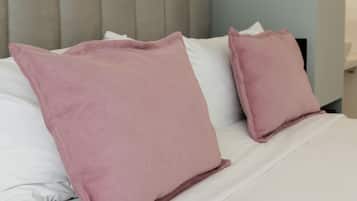 Una cama bien hecha con almohadas blancas y rosas, un cabecero azul claro y una lámpara fijada a la pared.