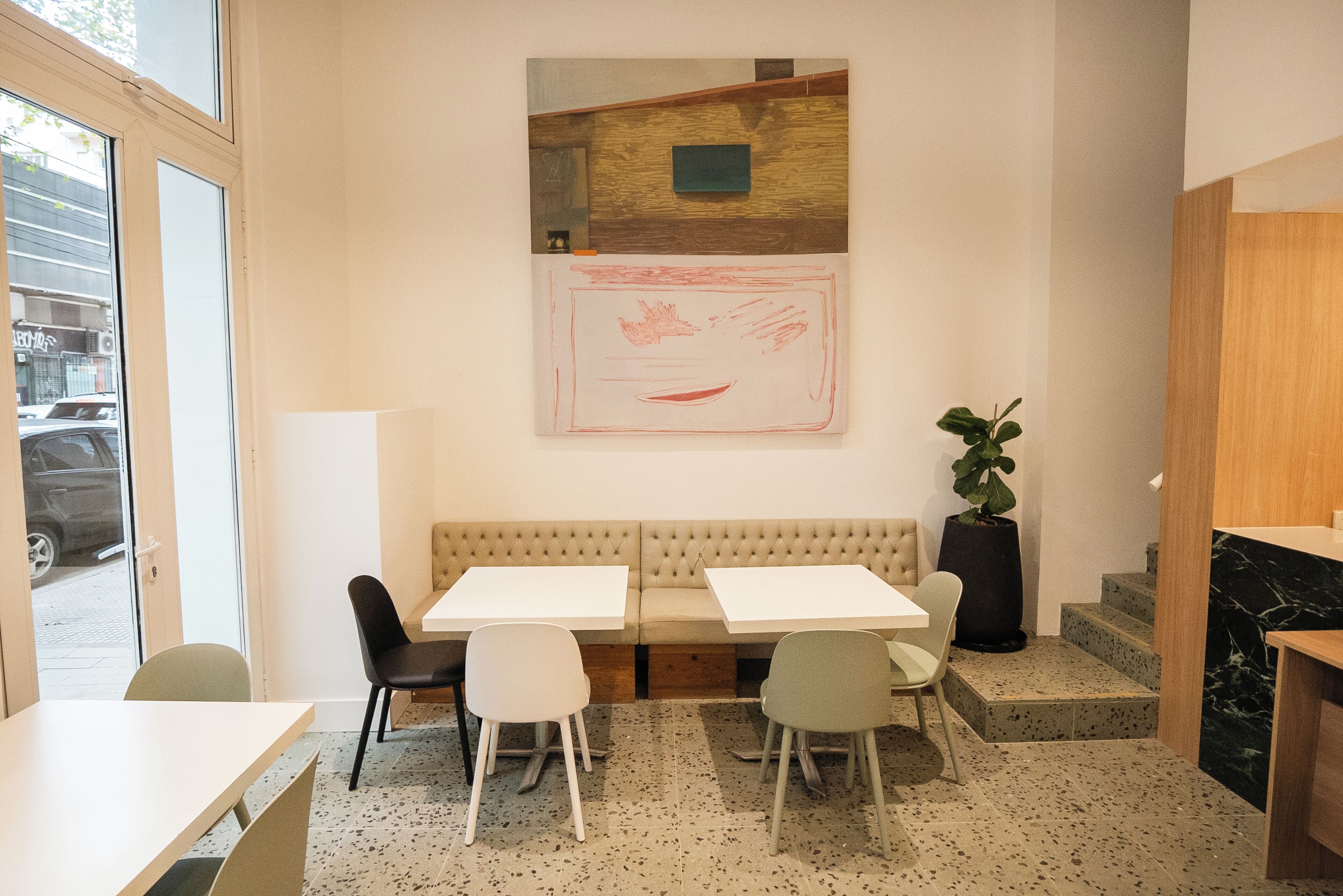 Un interior moderno con una zona de estar, dos mesas y un cuadro abstracto grande en la pared.