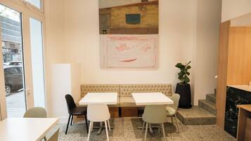 Un interior moderno con una zona de estar, dos mesas y un cuadro abstracto grande en la pared.
