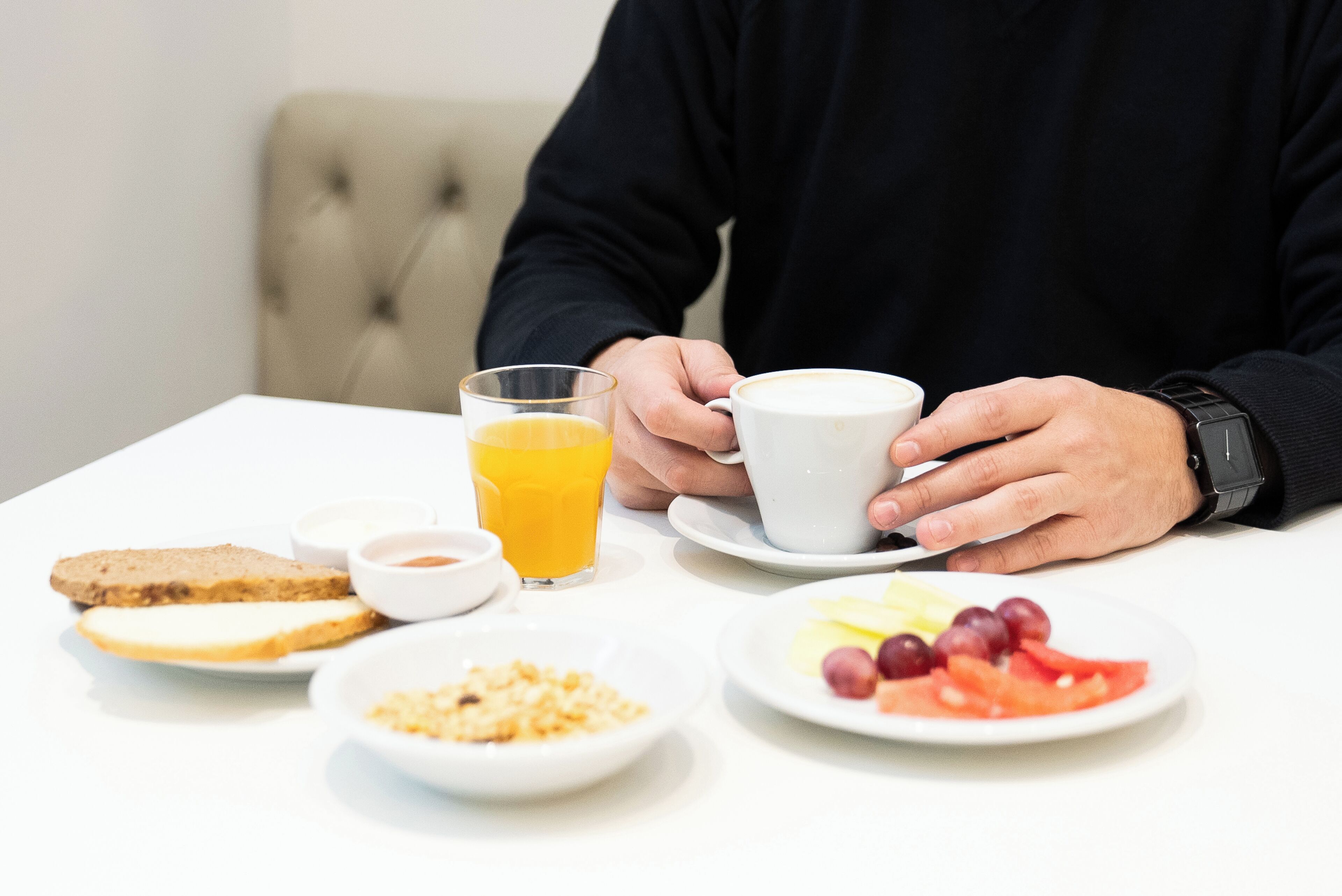 A breakfast setting with toast, cereal, fruit, a cup of coffee, and a glass of orange juice on a white table.