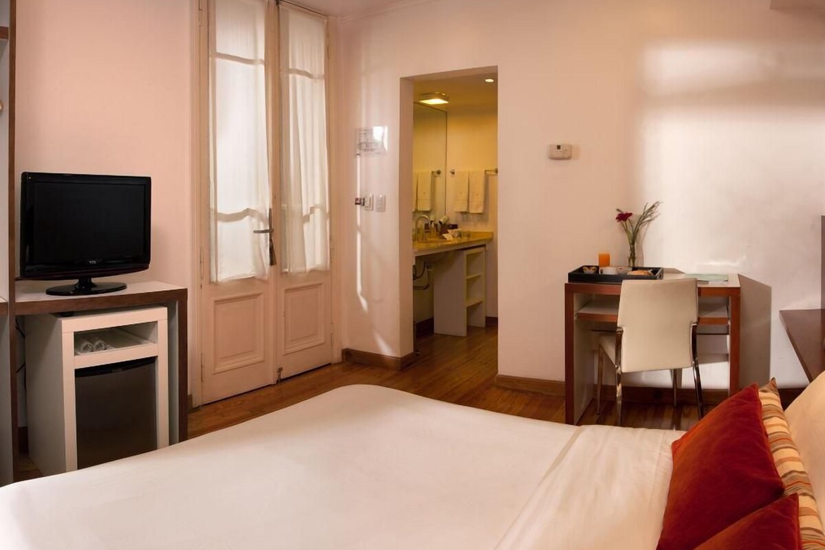 Habitación de hotel con cama, escritorio, televisor y kitchenette.