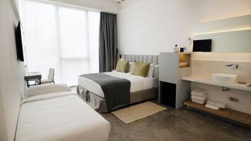 Una habitación de hotel moderna con una cama grande, una cama más pequeña, un escritorio y un baño con espejo y lavamanos.
