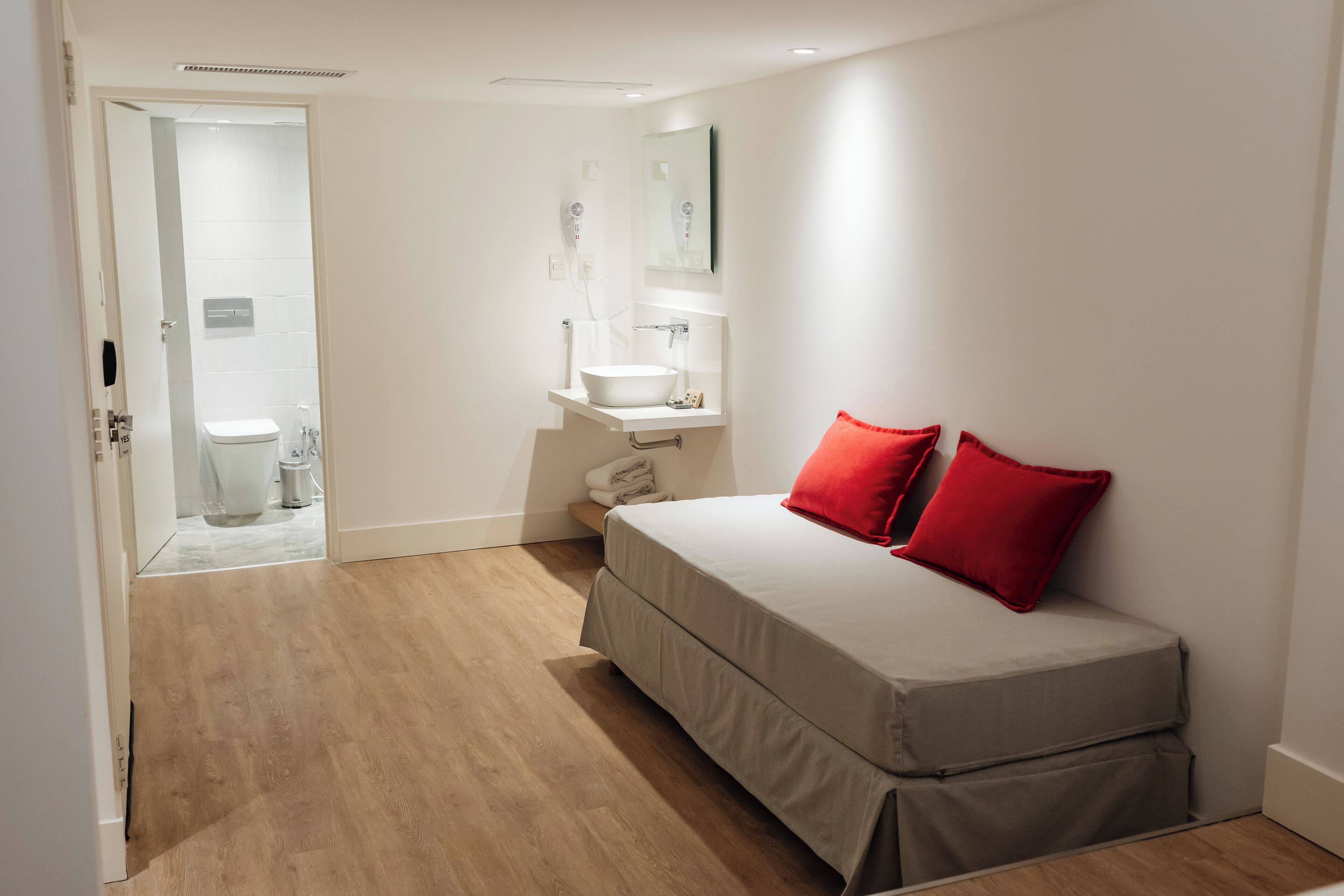 A bedroom with a bed, a nightstand, a mirror, and a bathroom visible through an open door.