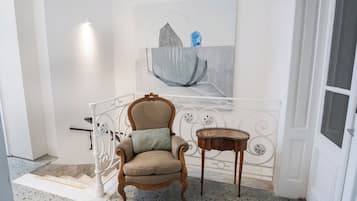 Een stoel met een kussen, een klein houten tafeltje en een schilderij aan de muur.