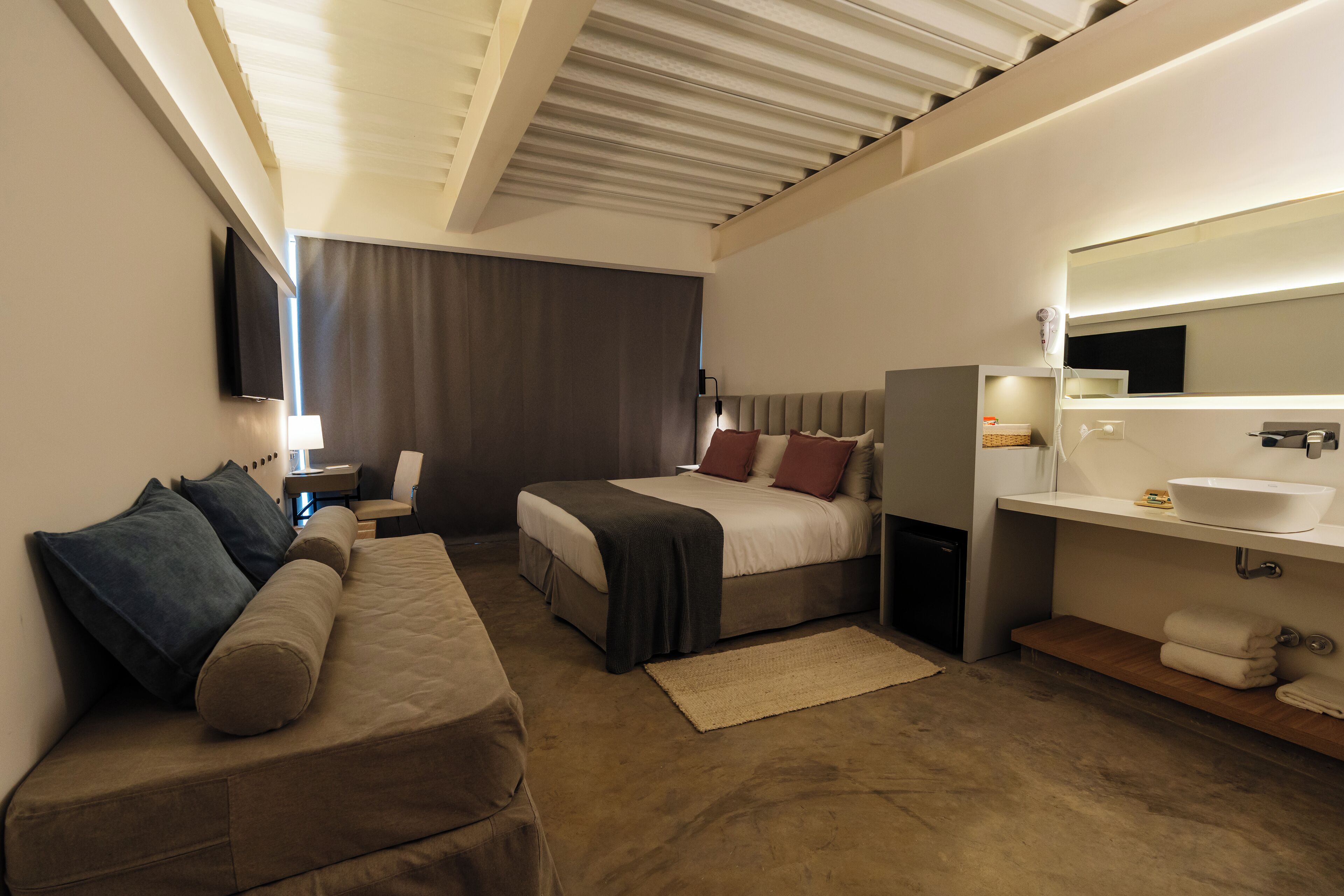 A modern hotel room with a bed, a sofa, a desk, and a bathroom.
