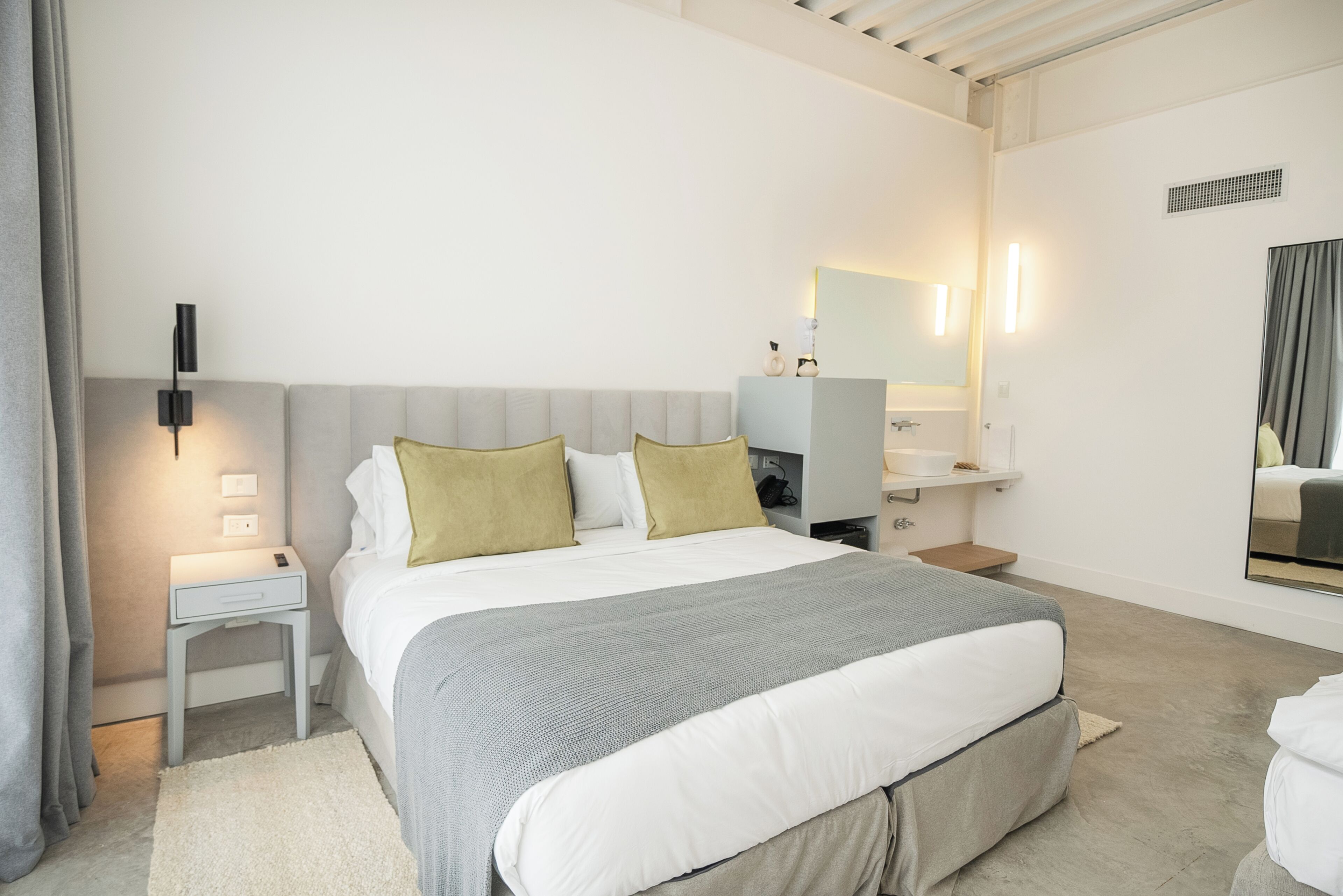 A modern bedroom with a large bed, bedside tables, a nightstand, a dresser, and a mirror.