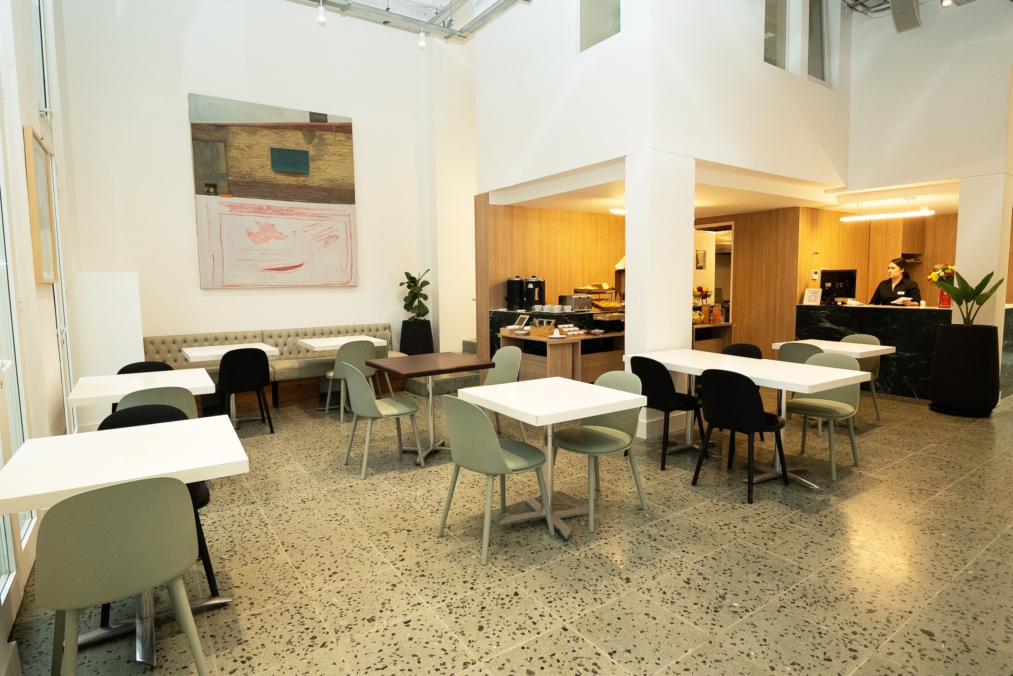 A spacious indoor area with multiple tables and chairs, a reception desk, and a kitchen area visible through an open doorway.