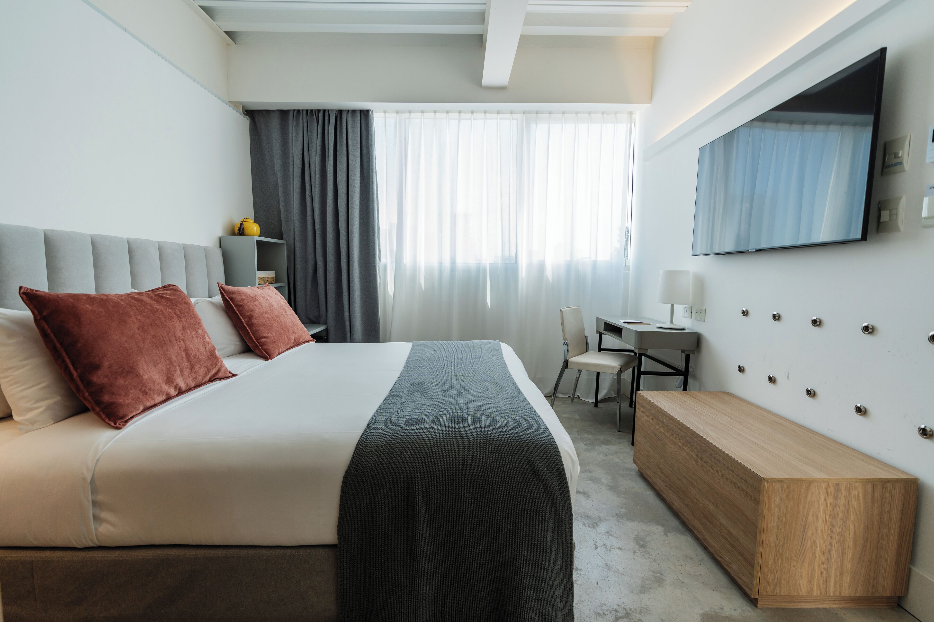 Una habitación de hotel moderna con una cama grande, un escritorio y un televisor fijado a la pared.