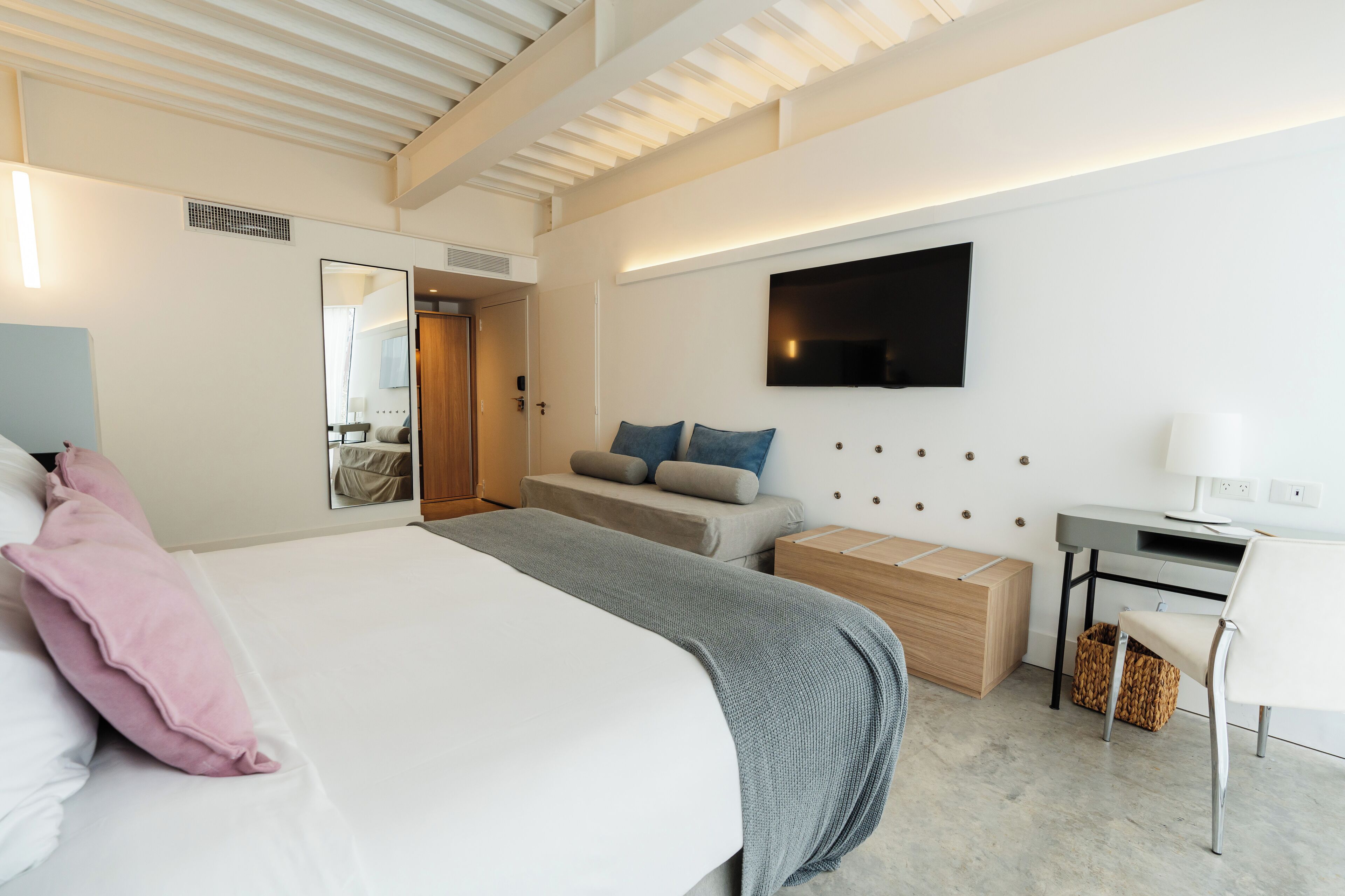 A modern hotel room with a large bed, a desk, a TV, and a seating area.