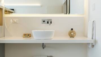A modern bathroom with a white sink, a mirror above it, and a wooden shelf below.