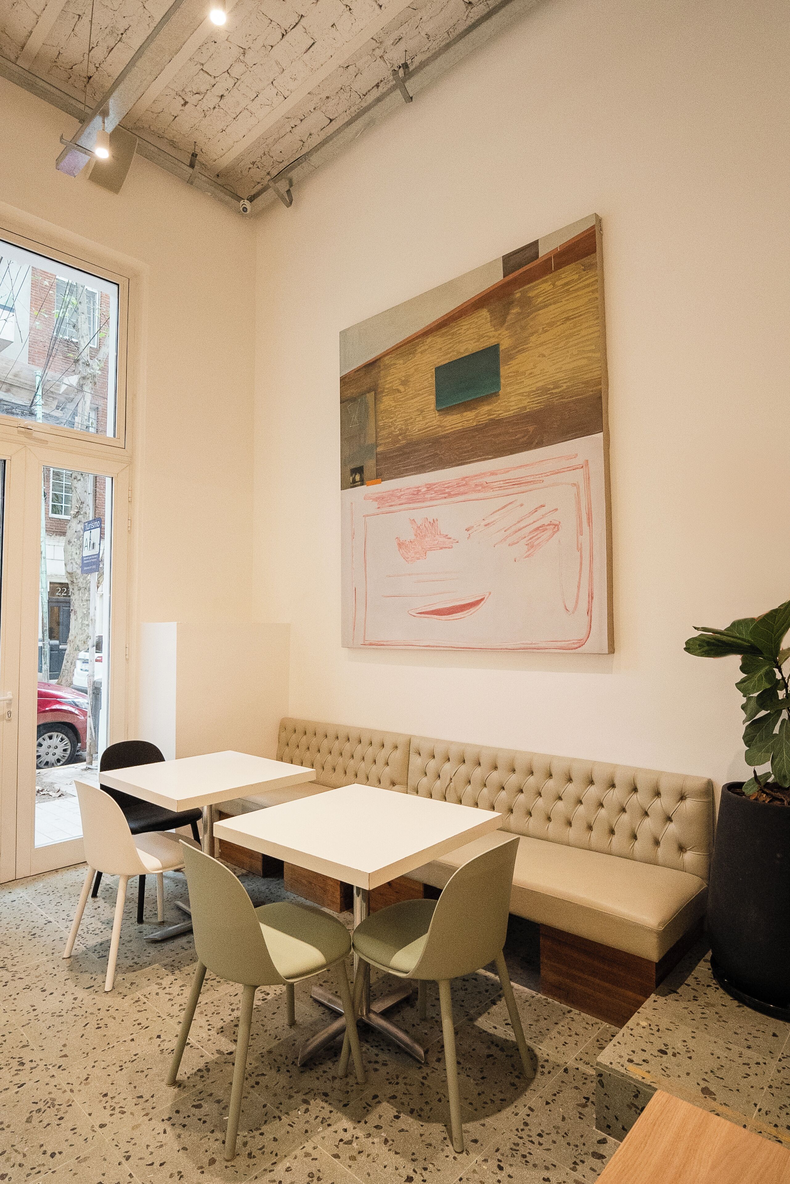 A modern interior with a beige sofa, two white tables, and green chairs.