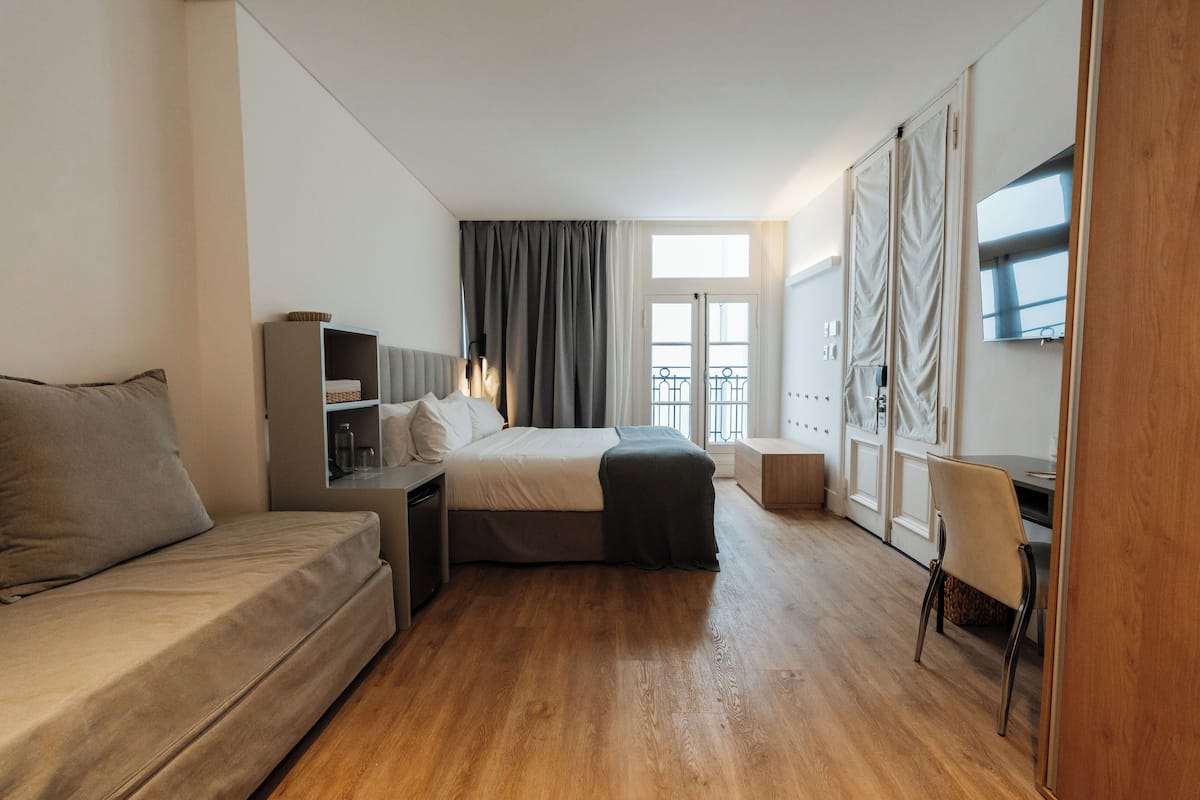 A modern hotel room with a bed, a sofa, a desk, and a chair.