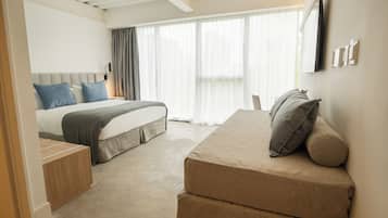 A modern hotel room with a bed, a sofa, and a TV on the wall.