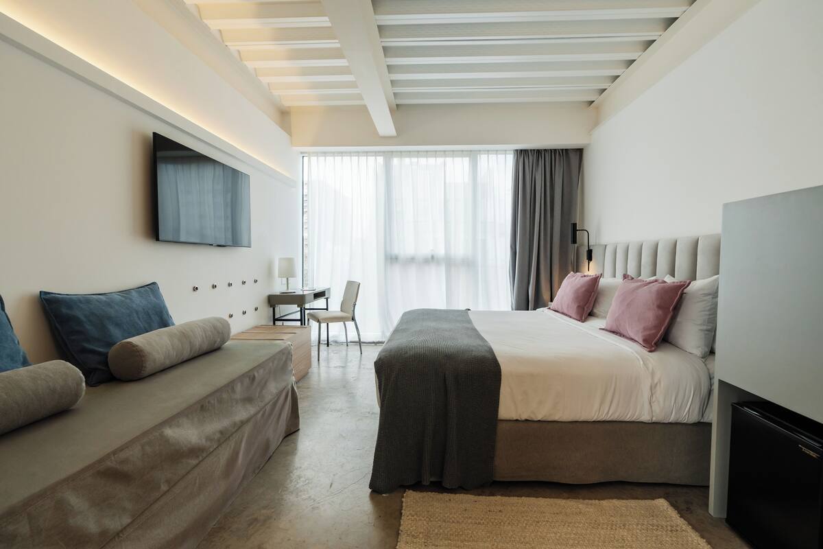 A modern hotel room with a bed, a sofa, a desk, and a TV.