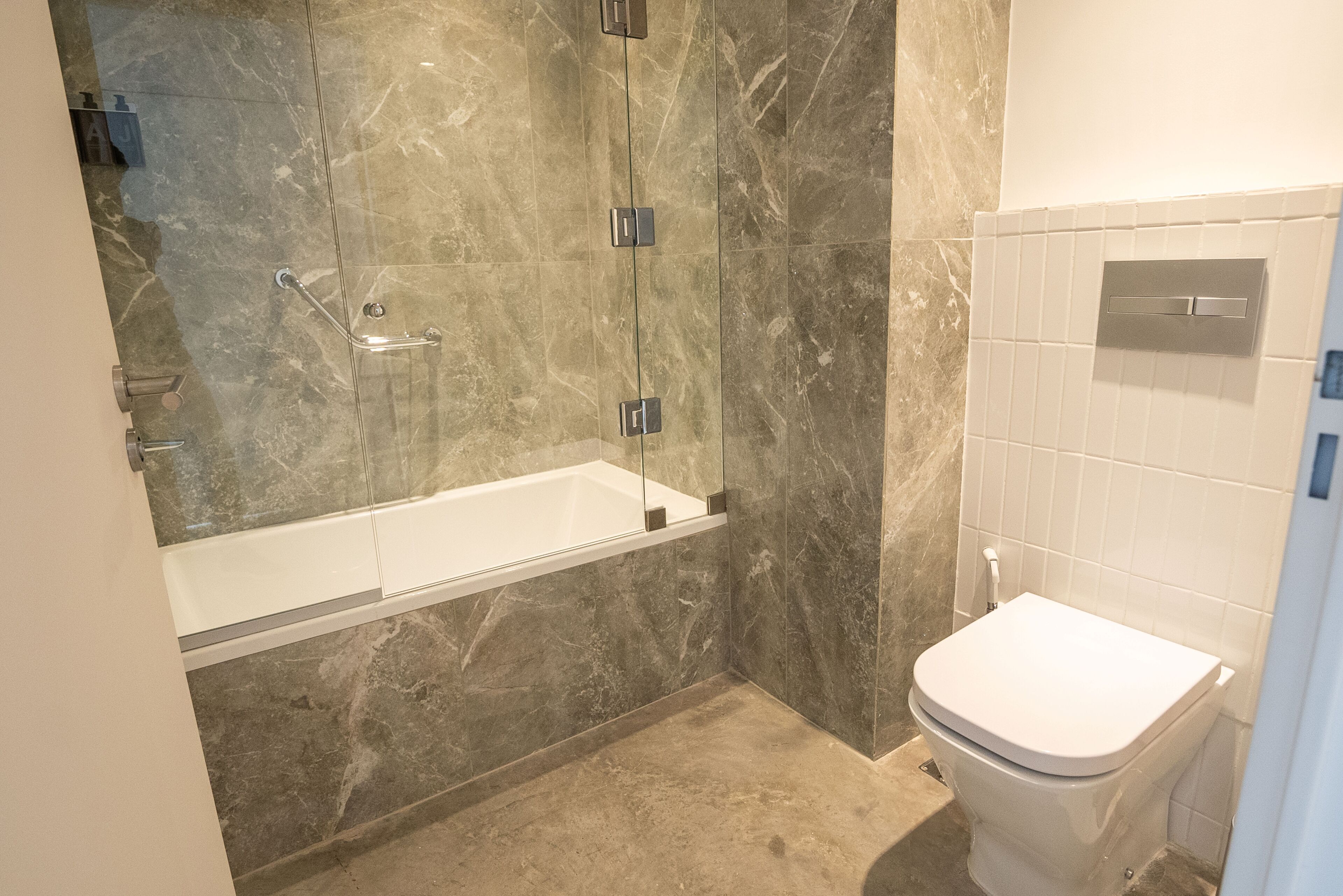 A modern bathroom with a glass-enclosed shower, a white toilet, and marble walls.