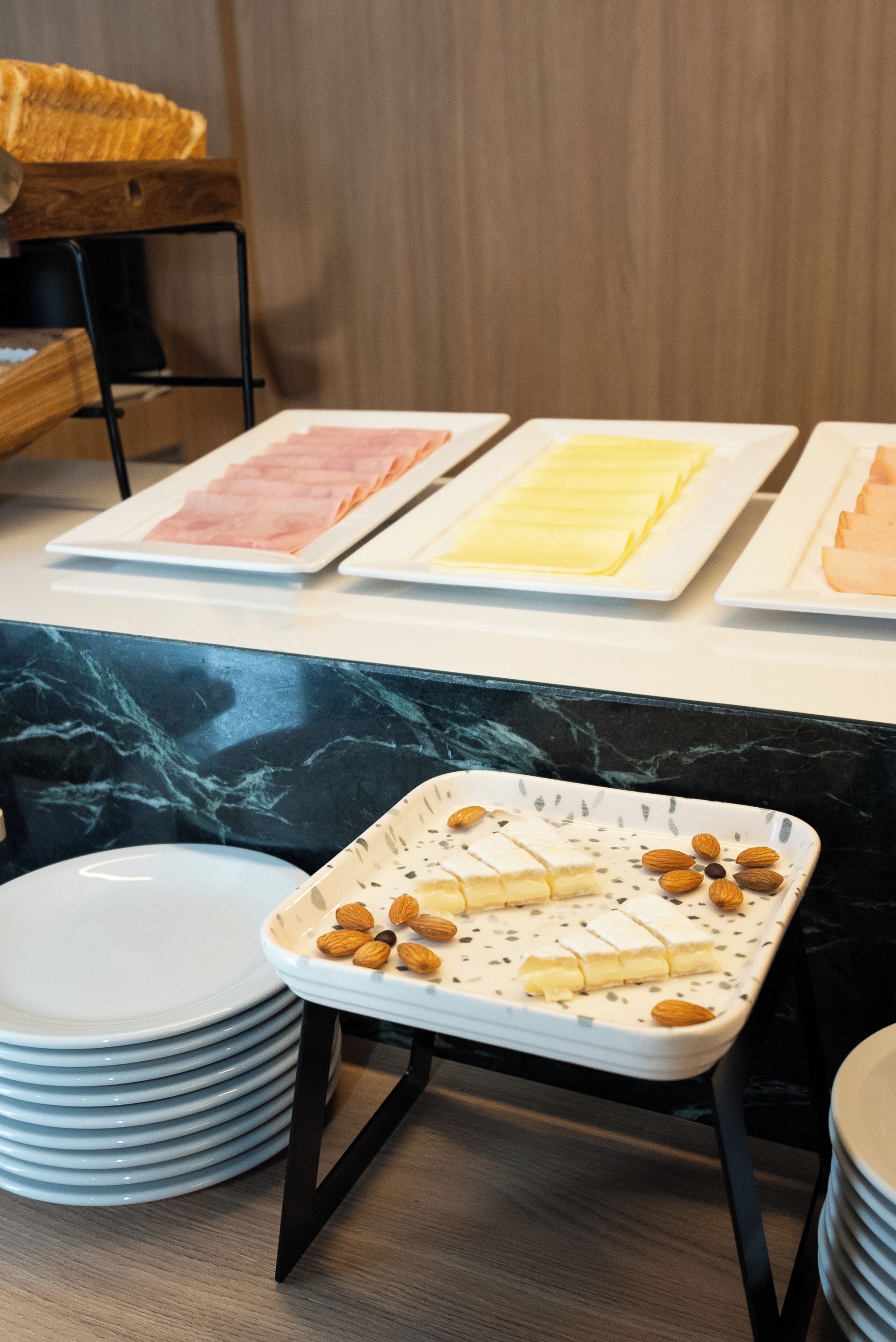Buffet montado com diversos alimentos em pratos, uma bandeja com amêndoas e uma pilha de pratos.