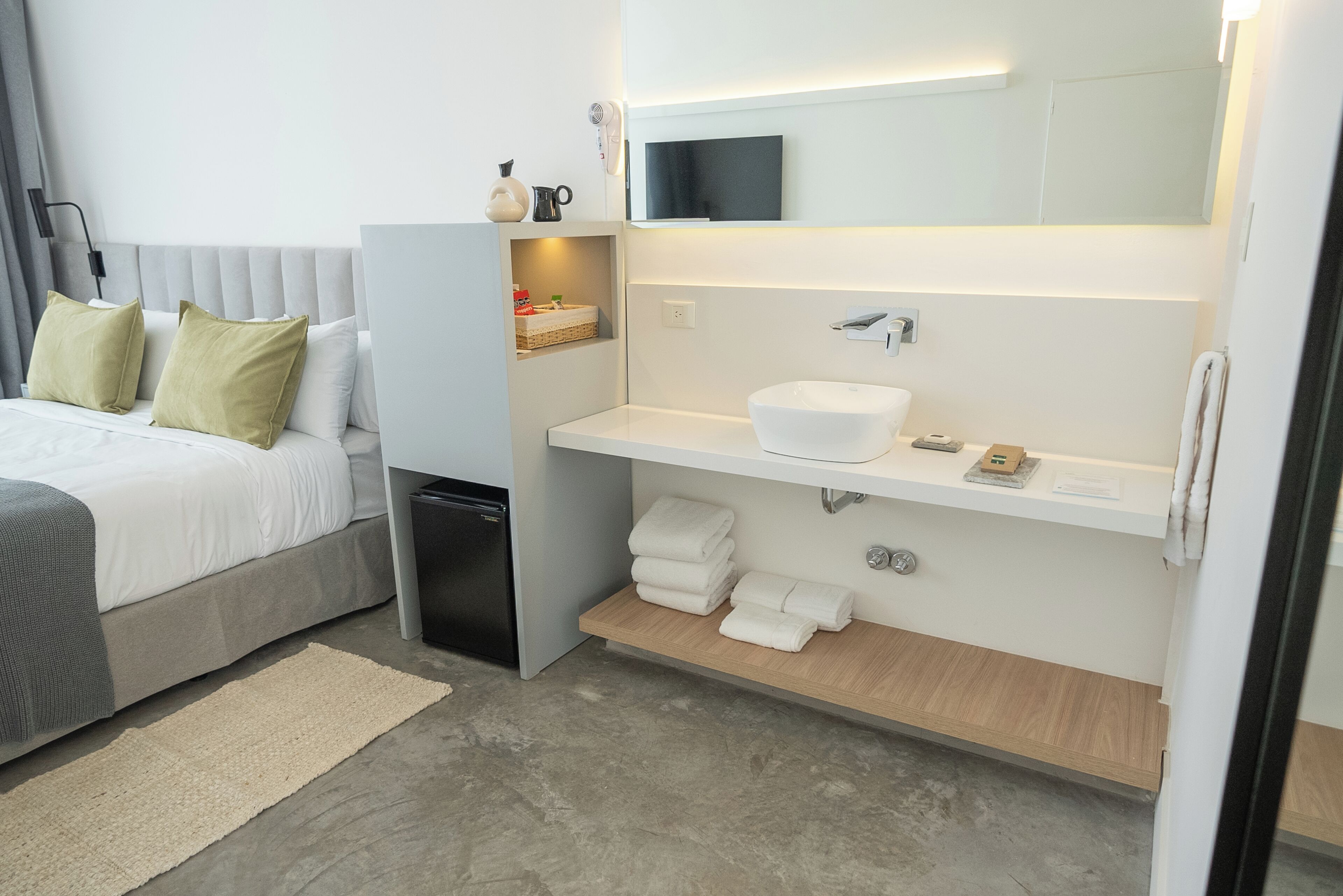 A modern hotel room with a bed, a built-in vanity, a hairdryer, and a flat-screen TV.