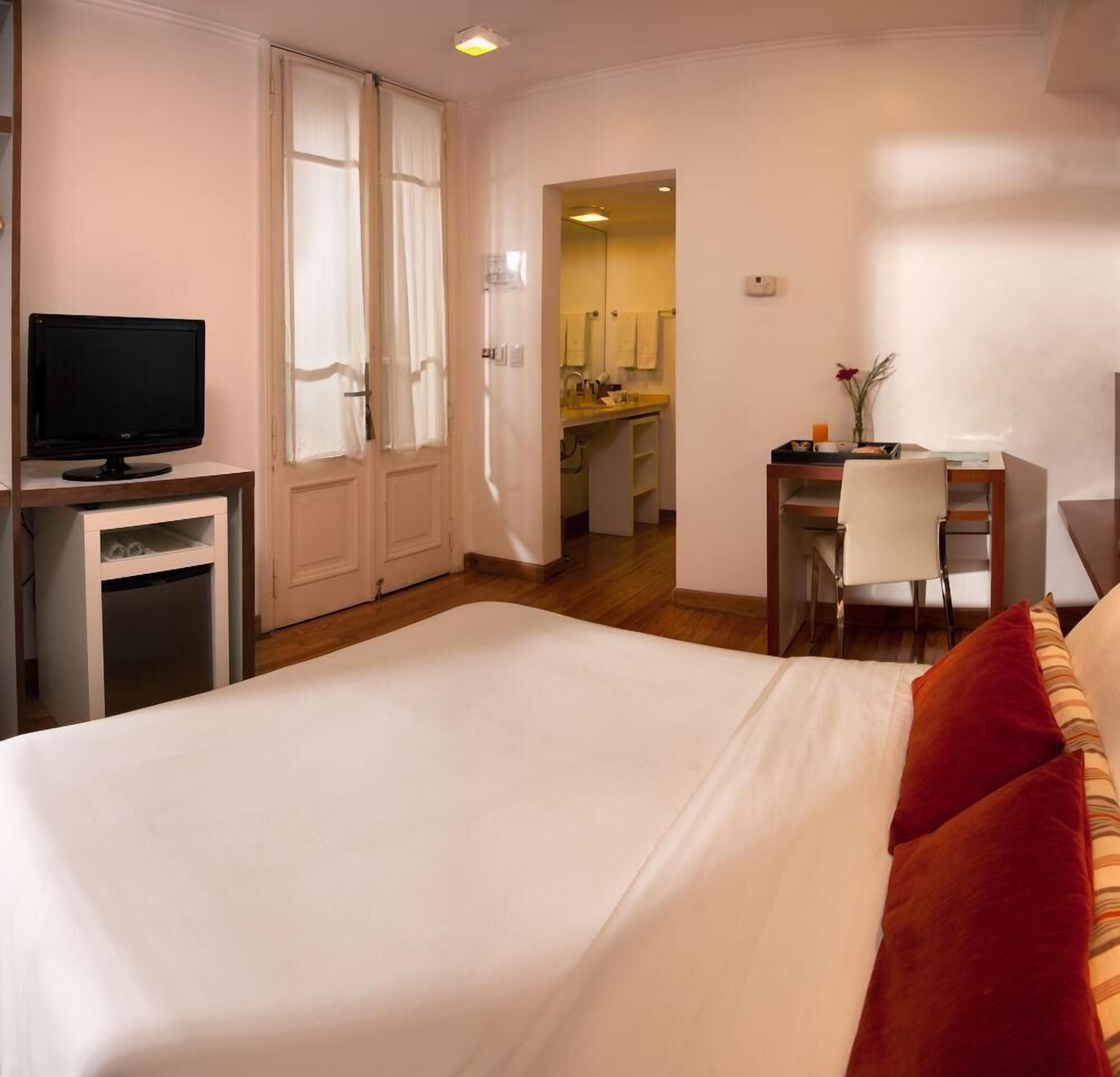 Habitació d'hotel amb llit, escriptori, televisió i petita cuina.