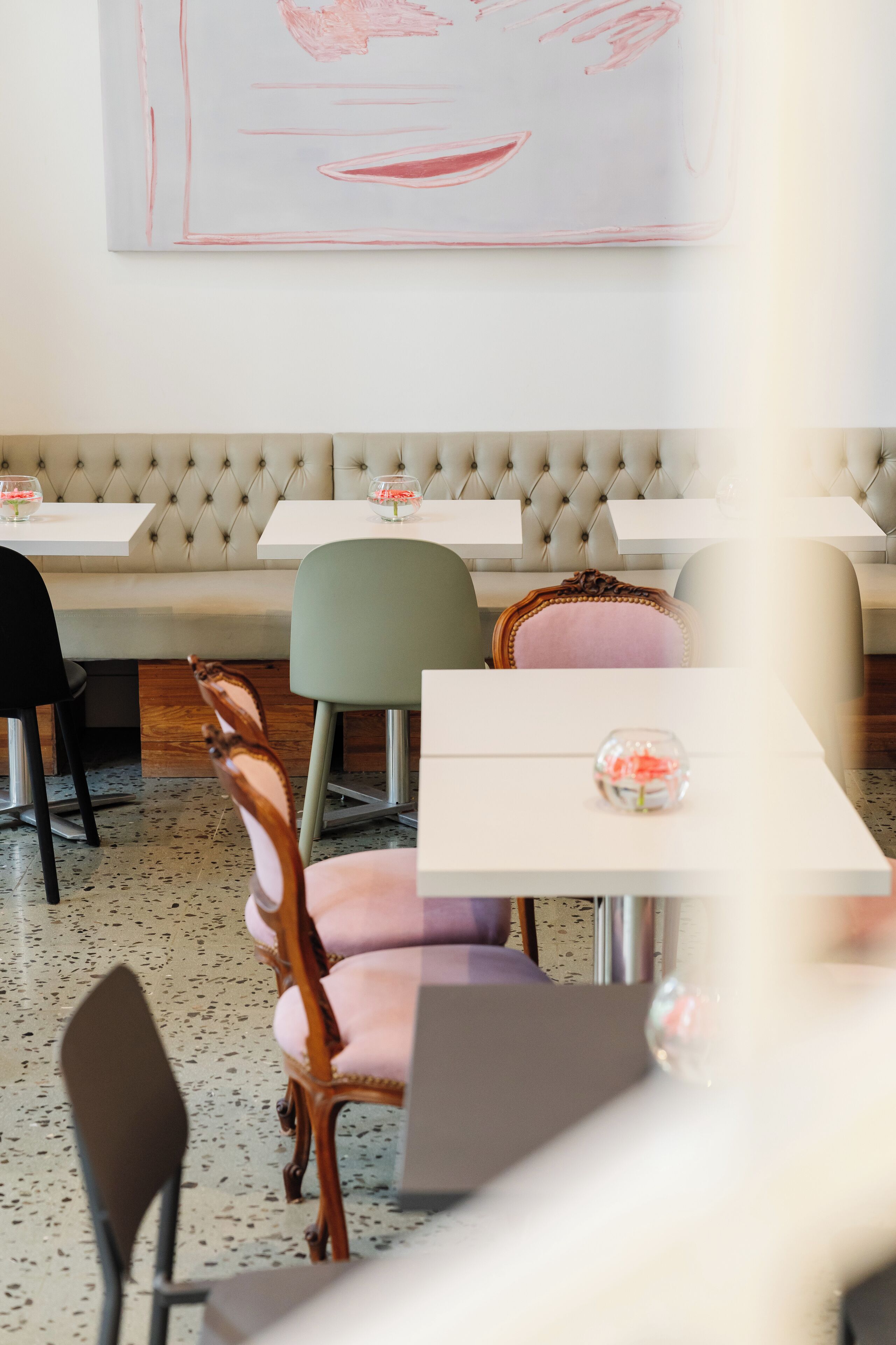 A restaurant interior with a tufted bench seating area, tables with chairs, and a wall-mounted abstract artwork.