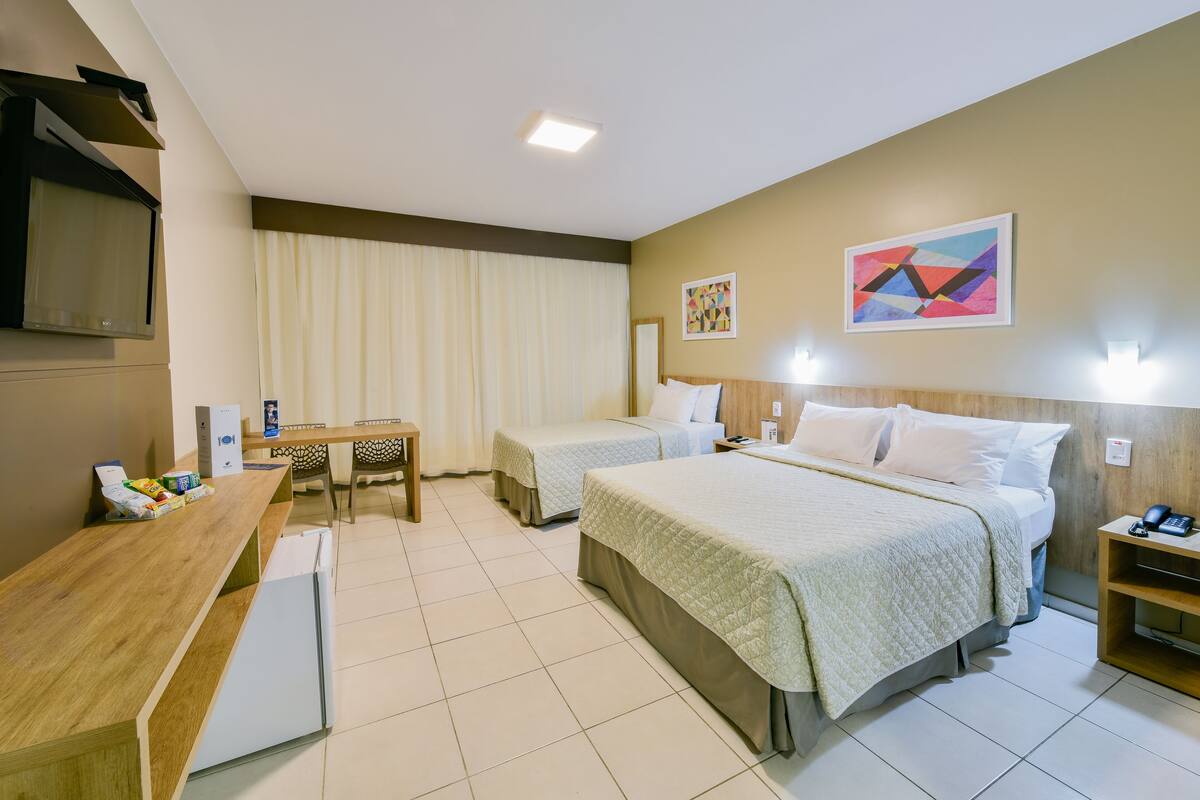 A hotel room with two beds, a desk, a refrigerator, and a TV.