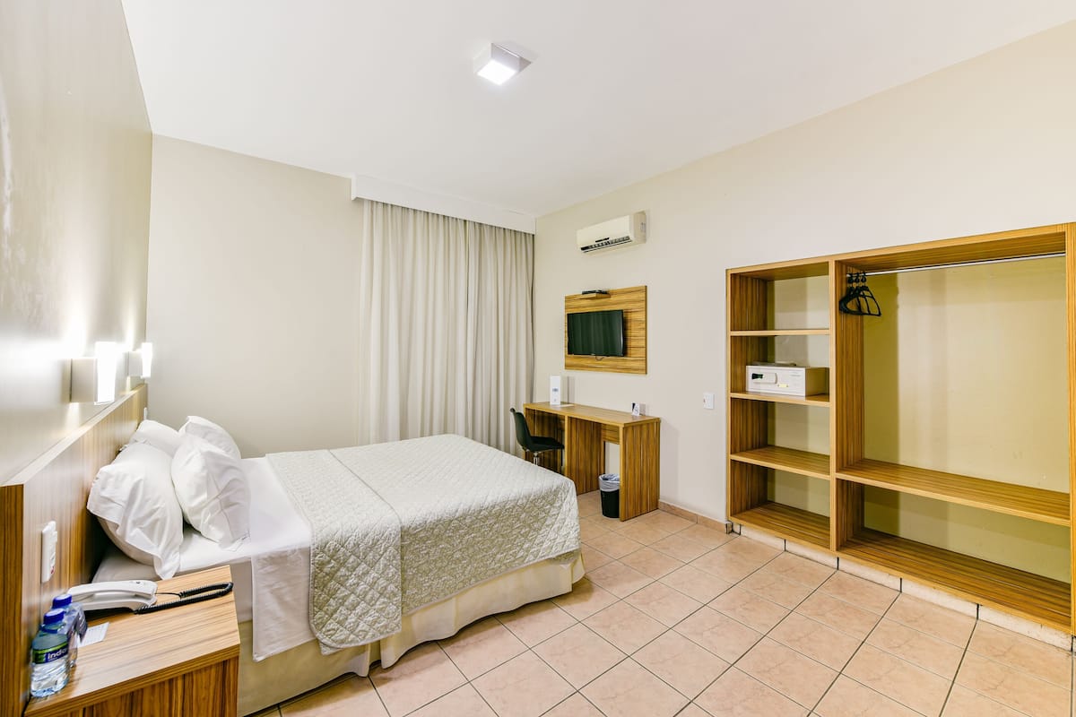 A hotel room with a bed, desk, chair, wardrobe, and a television.